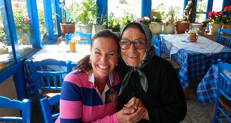 Deux femmes souriantes se tenant par la main à l'intérieur d'une taverne grecque colorée.