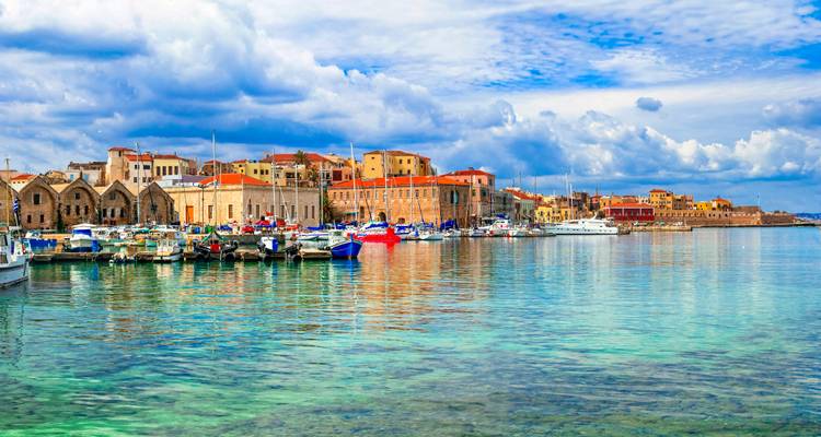 Le vieux port vénitien de La Canée avec des entrepôts en pierre se reflétant dans une eau turquoise cristalline.