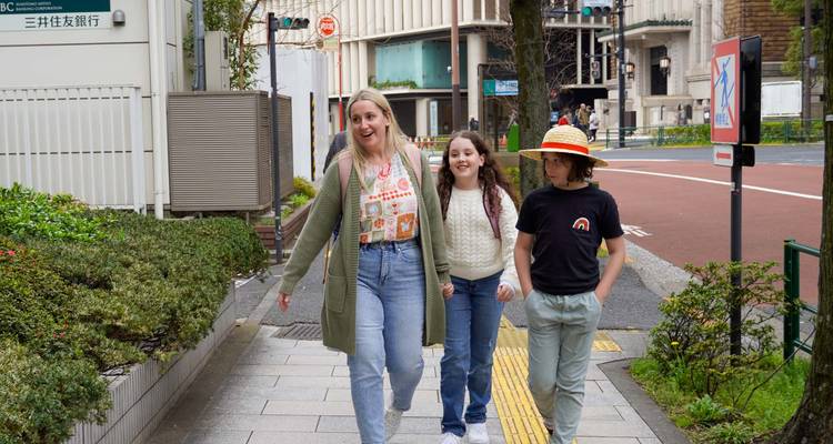 Una madre y dos niños pasean por una calle de Tokio, charlando felices entre edificios de la ciudad y mucha vegetación.