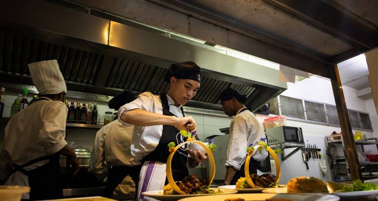 Los chefs en una cocina profesional emplazan cuidadosamente platos elaborados bajo campanas de ventilación de acero inoxidable.