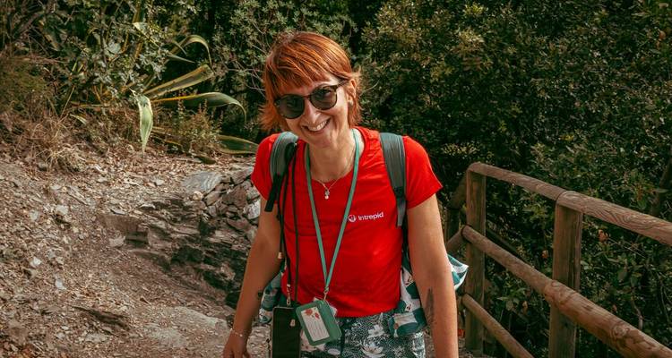 Guide souriant portant une chemise rouge Intrepid fait de la randonnée sur un sentier côtier rocheux avec un sac à dos et un cordon.