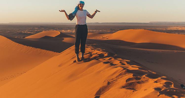 Une personne debout sur des dunes de sable avec une écharpe dans le désert au coucher du soleil.