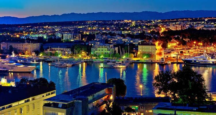 Vue du soir d'une ville côtière avec des lumières vives se reflétant sur l'eau.
