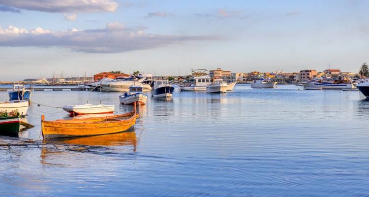 Los coloridos pequeños barcos de pesca descansan en un puerto tranquilo con un pueblo costero a lo largo del horizonte bajo la cálida luz de la tarde.