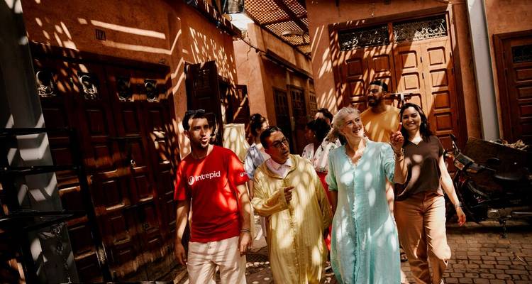 Guía intrépido conduce a los viajeros por el callejón de luz moteada de Marrakech con sombras geométricas en las paredes