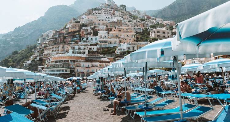 Crowded beach with hillside buildings and umbrellas.