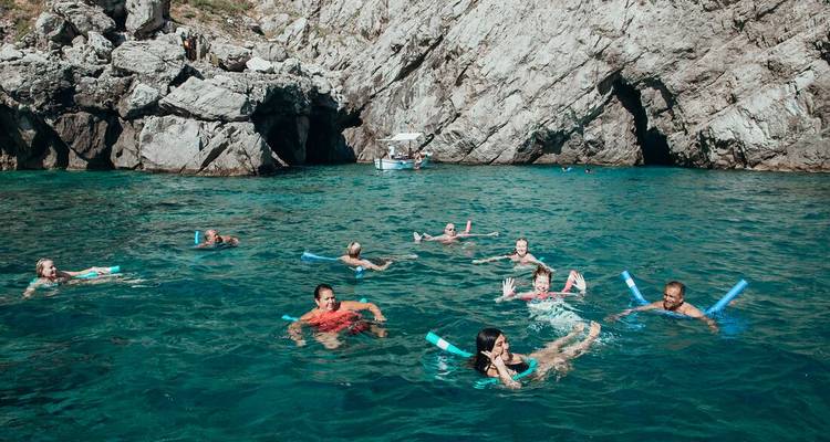 People swimming in clear blue water near rocky cliffs.