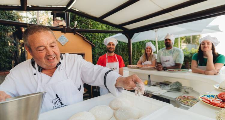 A man and tourists making pizza in an outdoor kitchen.