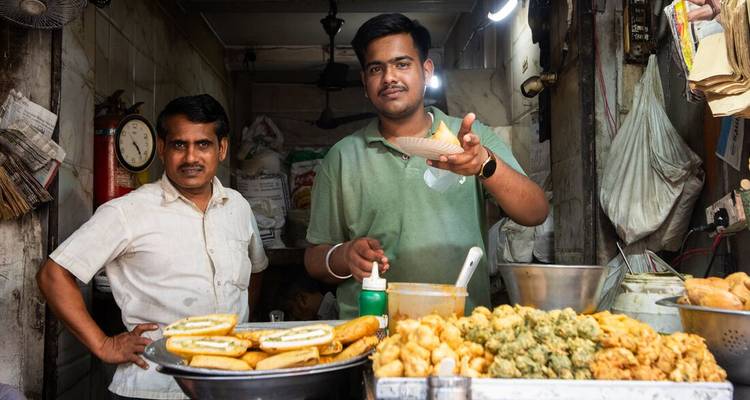 Twee mannen in een kleine voedselkraam die traditionele Indiase snacks aanbieden en bereiden.