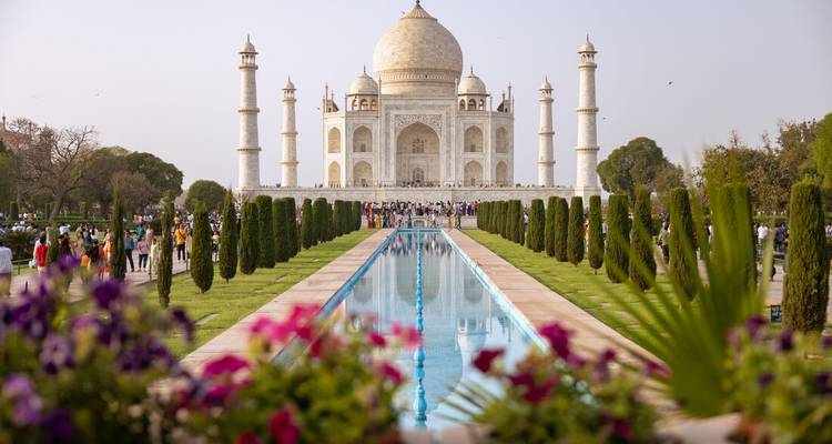 De Taj Mahal weerkaatsend in zijn lange vijver omzoomd door cipressen met bezoekers op de voorgrond.