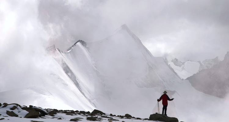 Personnage solitaire devant une montagne brumeuse aux sommets enneigés.