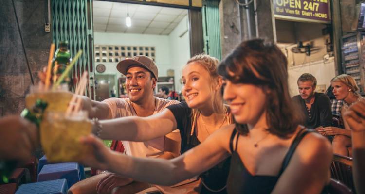 Un groupe d'amis qui trinque avec des boissons dans un marché nocturne animé.