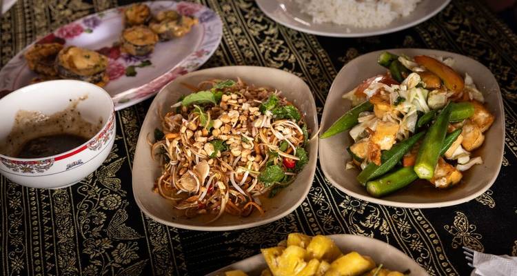 Gros plan de plusieurs plats cambodgiens sur un tissu à motifs : légumes sautés, salades et sauce d'accompagnement
