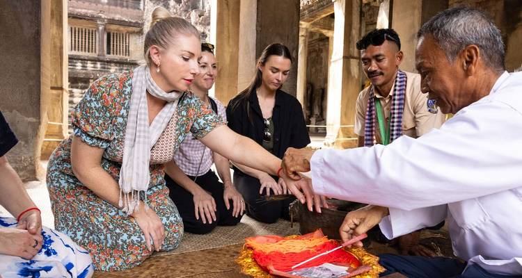 Un petit groupe reçoit une bénédiction traditionnelle à l'intérieur du complexe d'Angkor Vat, un moine attache une ficelle rouge au poignet d'un voyageur