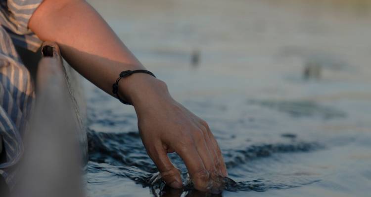 Une main traîne dans l'eau fraîche à côté d'un canoë en bois sur un chenal calme du delta.