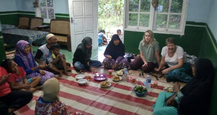 Group of people sitting on the floor sharing a meal inside a house.