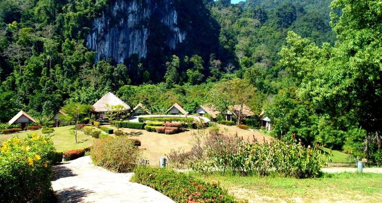 Resort ecológico tropical con cabañas de paja ubicadas en un exuberante valle verde rodeado de acantilados de piedra caliza y bosque denso.