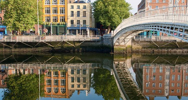 Le pont historique Ha'penny Bridge enjambe la rivière Liffey de Dublin, reflétant les bâtiments colorés du quai dans l'eau calme