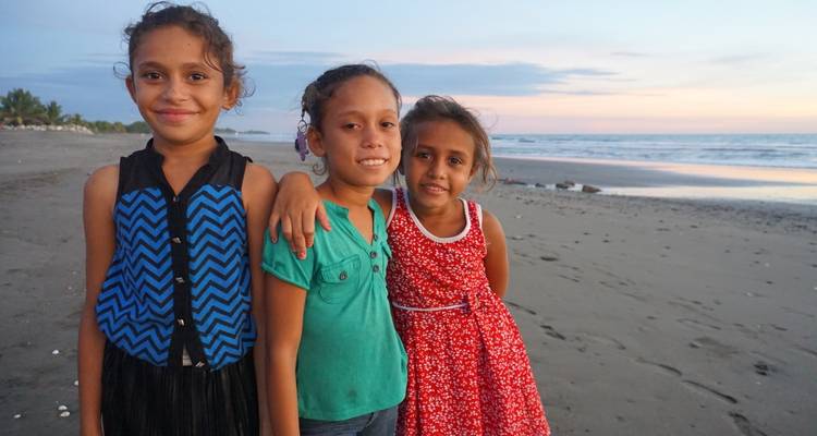 Trois filles posant sur une plage au coucher du soleil.