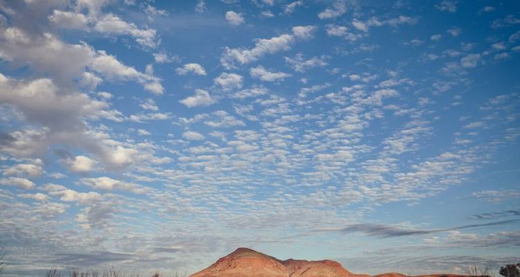 Una mesa roja solitaria se alza bajo un cielo vasto lleno de nubes dispersas como algodón.