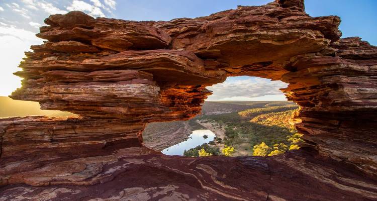 La luz del sol ilumina el arco de piedra arenisca roja de la Ventana de la Naturaleza que enmarca un valle fluvial abajo.