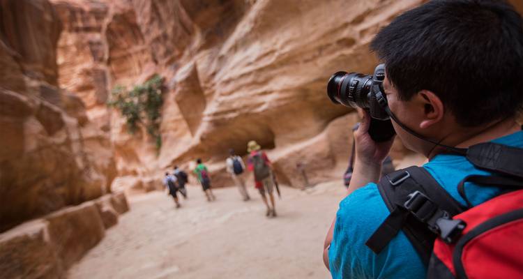 Los turistas caminan por el estrecho Siq de Petra mientras un fotógrafo en primer plano captura la escena.