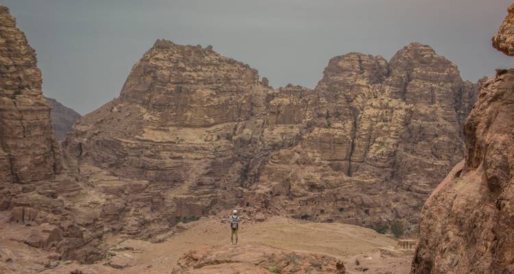 Un mochilero solitario de pie en una cornisa rocosa con vistas a dramáticas montañas de arenisca y cañones.