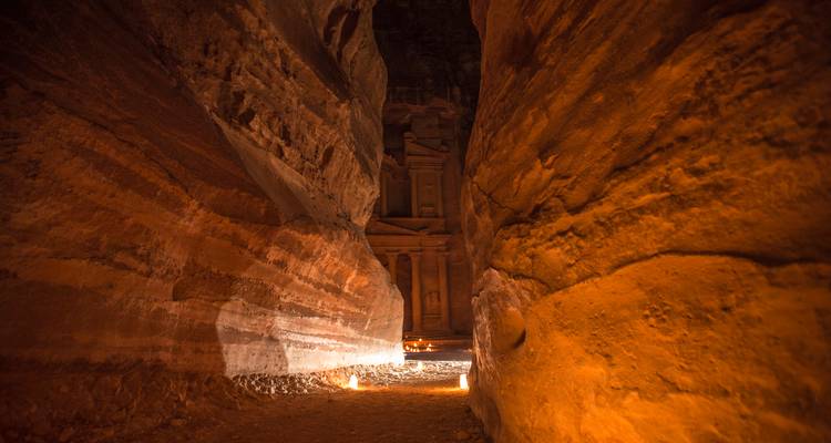 Un desfiladero de arenisca iluminado con velas revela un vistazo al icónico Tesoro de Petra por la noche.