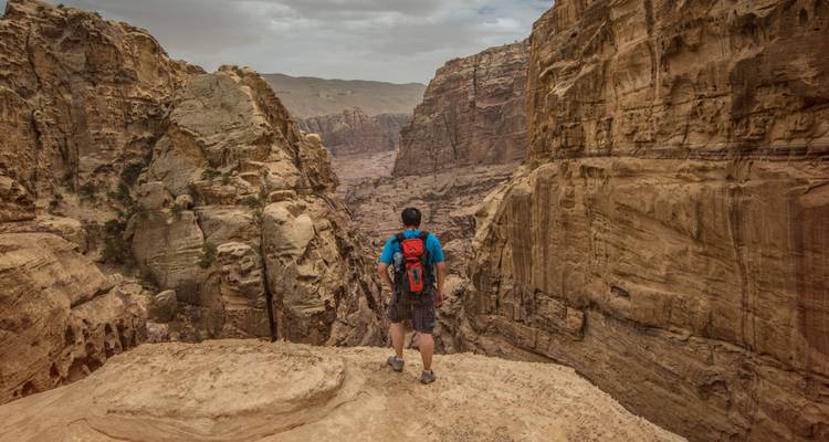 Un aventurero con una mochila roja mira hacia un paisaje de cañón de arenisca escarpado.