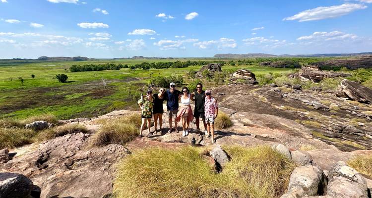 Un petit groupe de voyageurs se tenant sur un escarpement rocheux surplombant de vastes plaines vertes et des zones humides dans le Parc national de Kakadu.