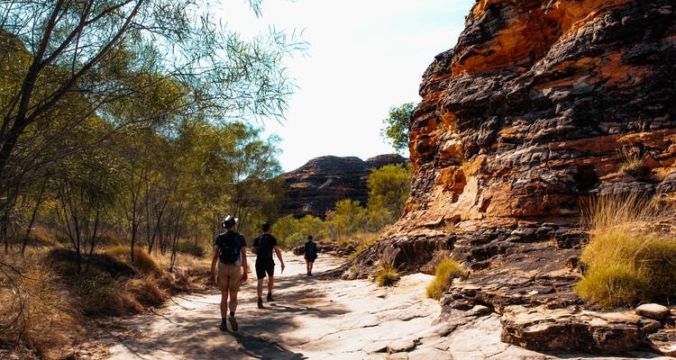 Des promenades en groupe à travers une gorge rocheuse aux parois de grès rayé sous un ciel dégagé.