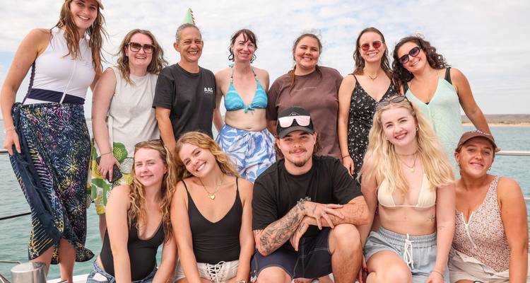 Group portrait on a boat deck with ocean views on a lightly overcast day.