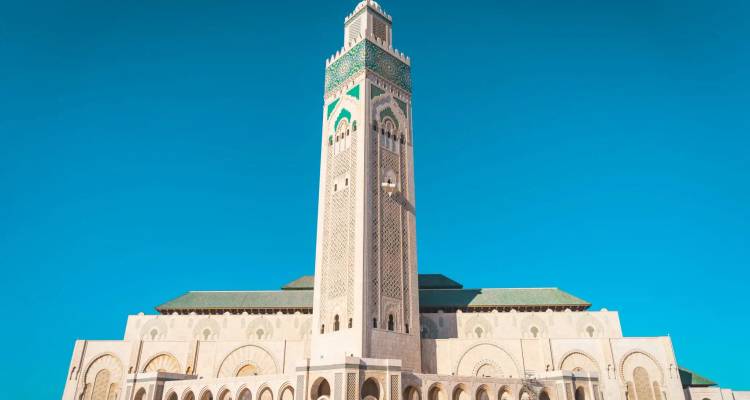 Gesamte Fassade der Hassan-II.-Moschee mit ihrem aufragenden Minarett vor einem wolkenlosen Himmel.