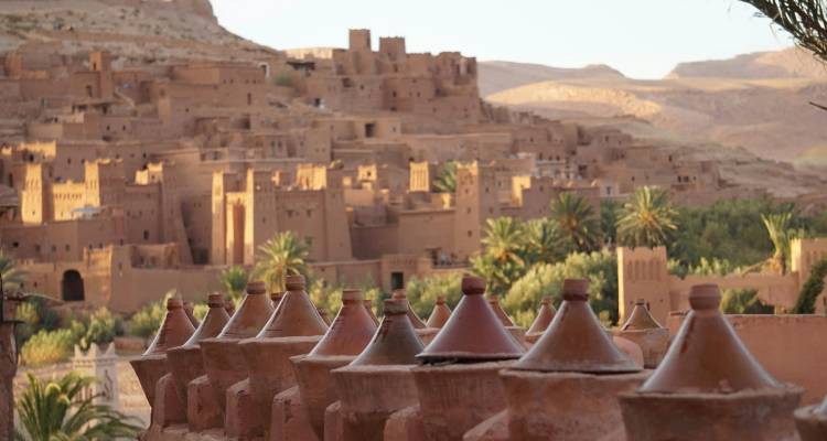 Des couvercles de tajines en terre cuite au premier plan avec l'ancien village en terre d'Aït Benhaddou sur la colline à l'arrière-plan.