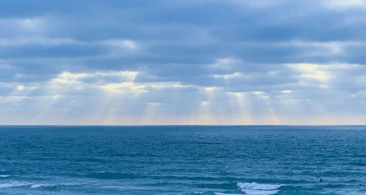 Vaste étendue d'eau océanique calme sous des nuages gris-bleu en couches avec des rayons de soleil perçant à travers.