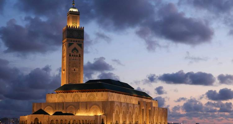 La Mosquée Hassan II illuminée au crépuscule sous un ciel dramatique strié de nuages, sur la côte atlantique.