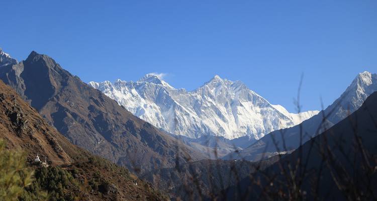 Helder uitzicht op de glinsterende Everest en Lhotse massief omgeven door bruine lagere bergkammen onder een diepe blauwe hemel.