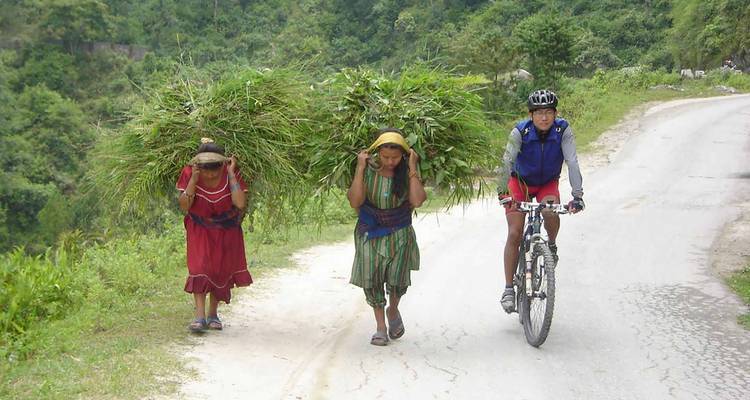 Fietser passeert dorpelingen die gras dragen op een plattelandsweg.