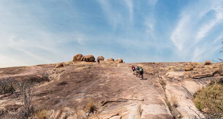 Kleingruppenwanderung auf einem breiten Granitabhang mit verstreuten Felsblöcken unter blauem Himmel