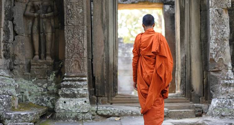 Moine bouddhiste en robes safran marchant à travers une ancienne porte de temple en pierre au milieu des ruines d'Angkor.