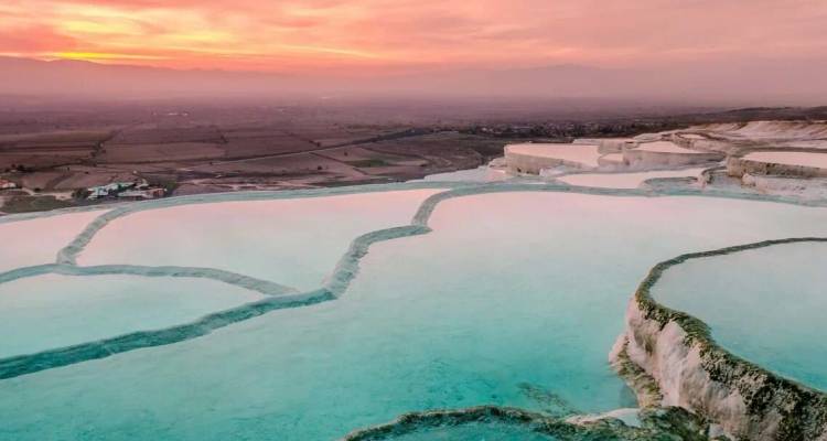 Le coucher de soleil aux teintes pastel projette sa lumière sur les bassins turquoise en escalier des terrasses de travertin de Pamukkale.