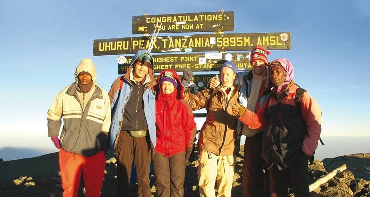 Wanderer feiern auf dem Gipfel des Uhuru Peak mit einem Schild.