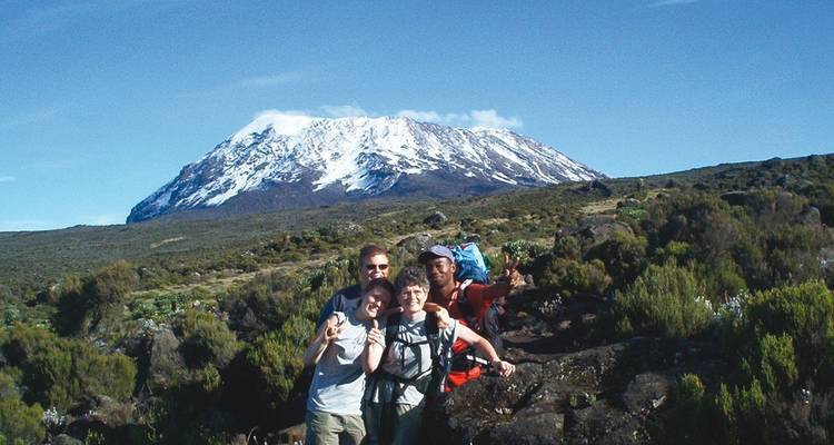 Happy trekking group posing with snow-capped Mount Kilimanjaro rising behind them