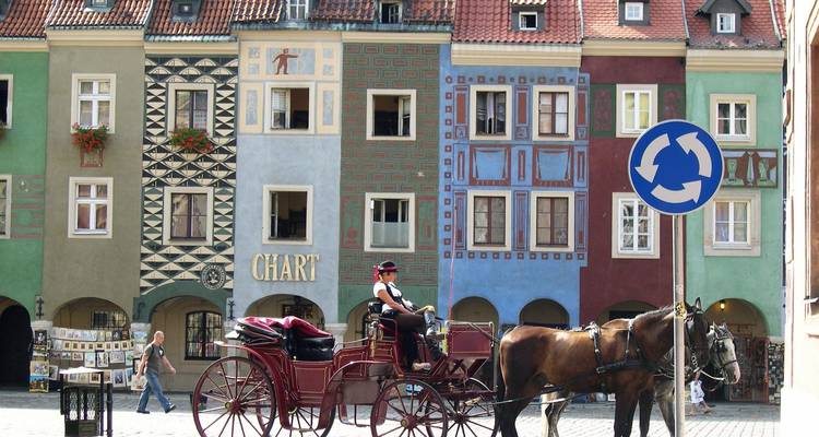 Edificios coloridos y un carruaje tirado por caballos en una plaza histórica.