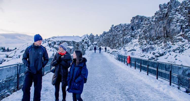 Los viajeros caminan por un sendero nevado del cañón bordeado por paredes rocosas en Thingvellir