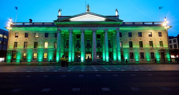 La histórica Oficina General de Correos en la calle O'Connell iluminada con luz verde al anochecer con un cielo azul claro.