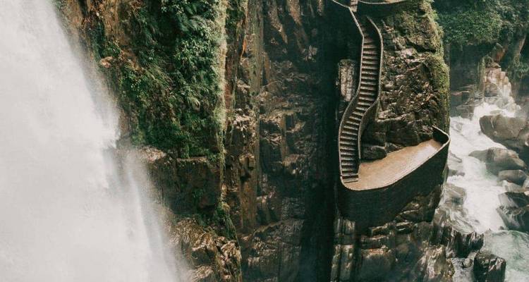 Escalera de piedra empinada agarrada a un acantilado junto a una poderosa cascada tropical.