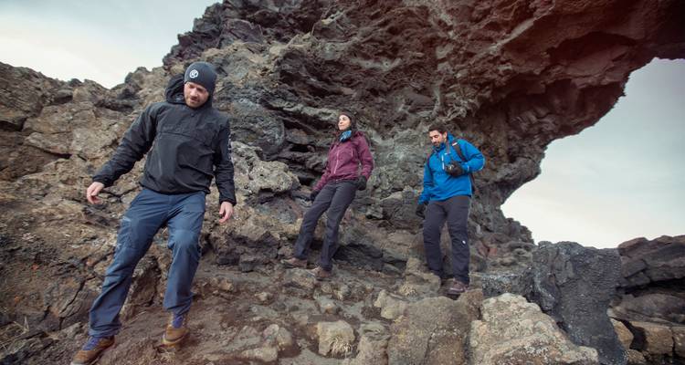Trois trekkeurs explorent des formations rocheuses volcaniques accidentées et des arches naturelles dans les champs de lave d'Islande.