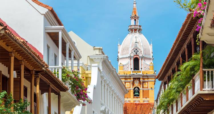 Malerische Kolonialstraße mit Balkonen, die die ikonische Kuppel der Kathedrale von Cartagena gegen einen blauen Himmel rahmen.