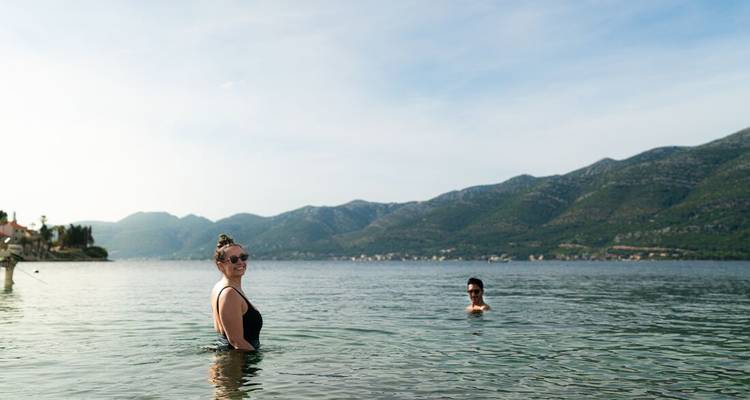 Dos personas nadando en un lago cristalino con montañas de fondo.